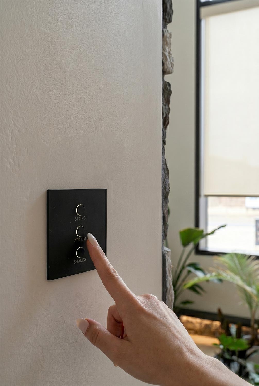 Hand pressing a button on a sleek black wall keypad to control lights and shades