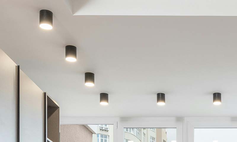A row of black cylindrical surface-mounted downlights on a white ceiling