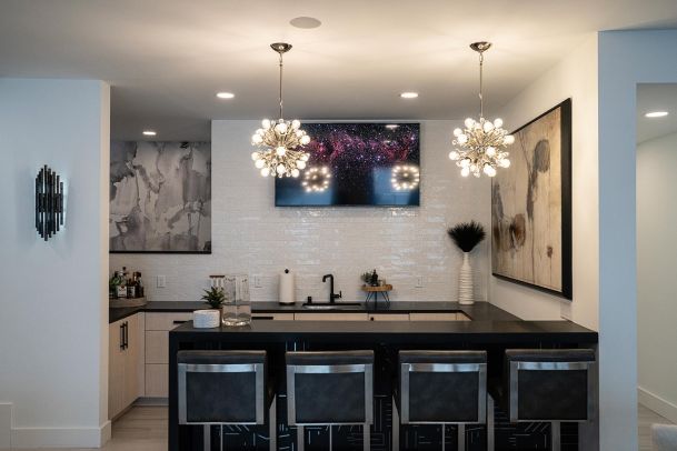 Modern home bar with starburst pendant lights and a television mounted on a tile wall