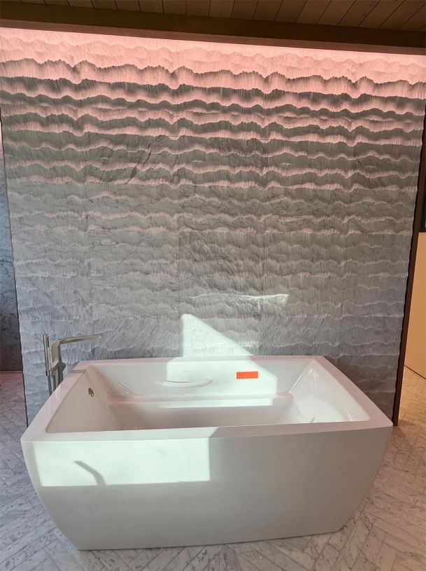 White freestanding soaking bathtub set against a textured wave-pattern gray stone wall