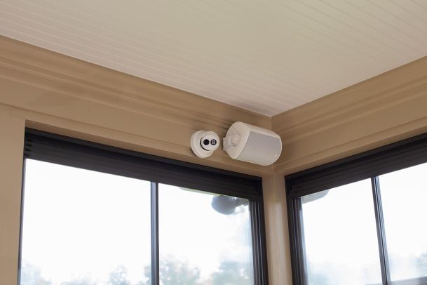 Security camera and white speaker mounted in the corner of a sunroom ceiling