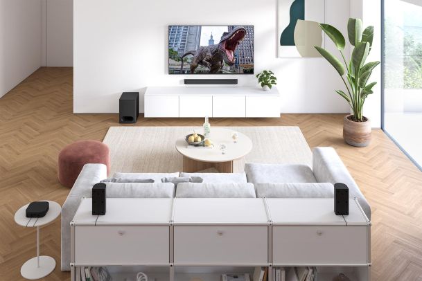 Living room with a dinosaur on TV and several small black speakers on white cabinets