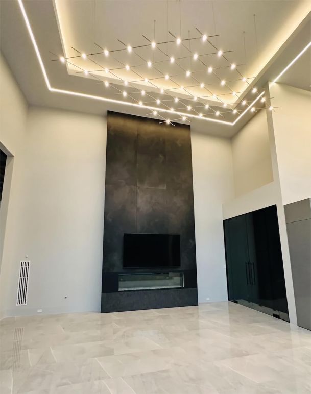 Large minimalist living room featuring a tall dark fireplace accent wall and a grid chandelier