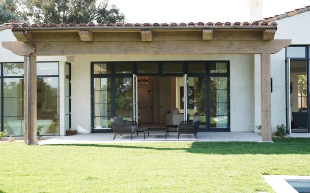 Covered patio with modern furniture and large glass doors leading into a luxury home