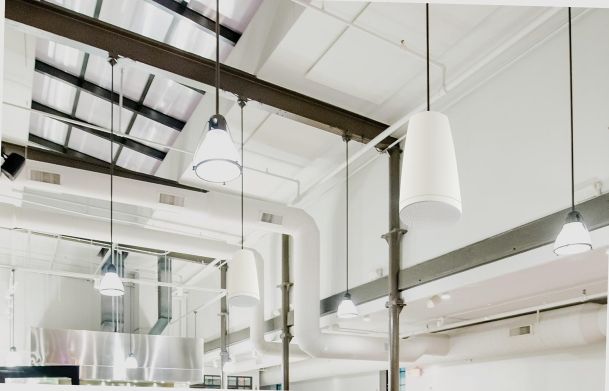 White cone-shaped pendant speakers and lights hanging from a high industrial ceiling