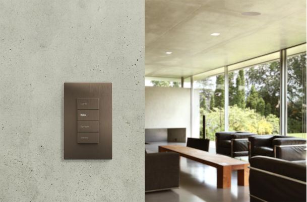 Bronze smart lighting keypad mounted on a textured wall overlooking a modern lounge