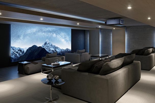 Dark modern theater room with grey sofas and a large screen showing snowy mountains