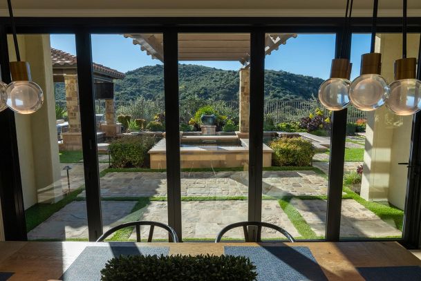 View through glass doors of a stone patio with a water feature and hills in the distance