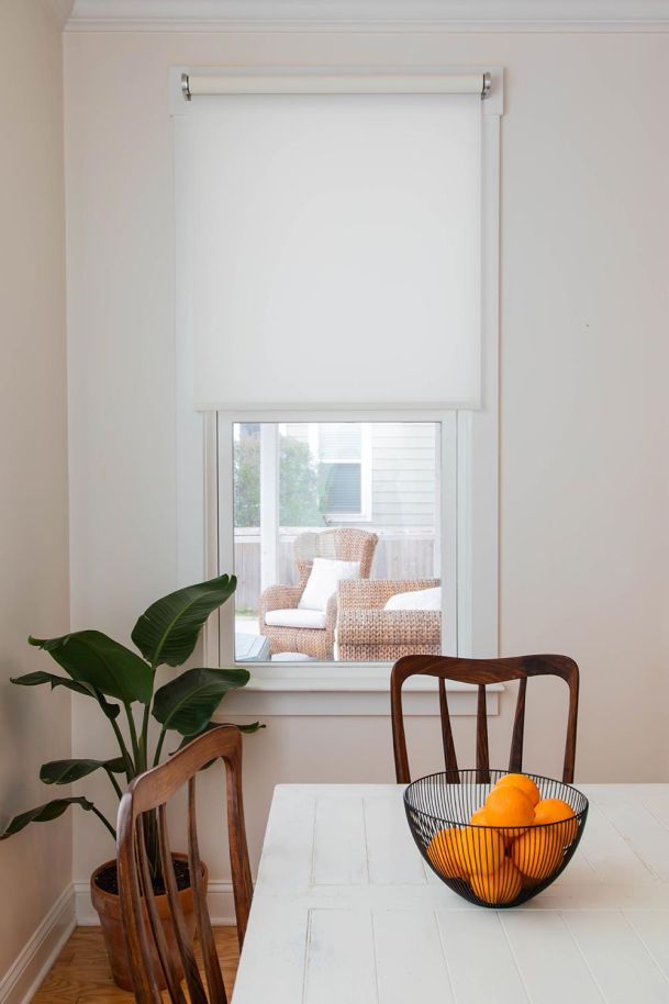 Close-up of a white window shade partially lowered in a bright breakfast nook