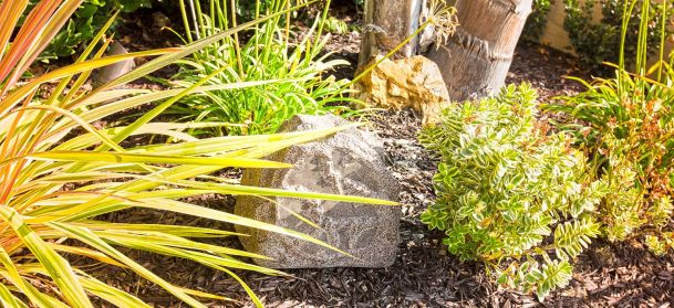Outdoor rock speaker camouflaged in a garden with mulch and various plants