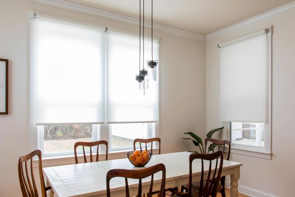 Dining room table with white roller shades on windows and pendant light fixture
