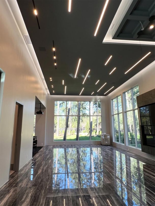 Expansive room with highly polished dark tile floor reflecting recessed linear ceiling lights