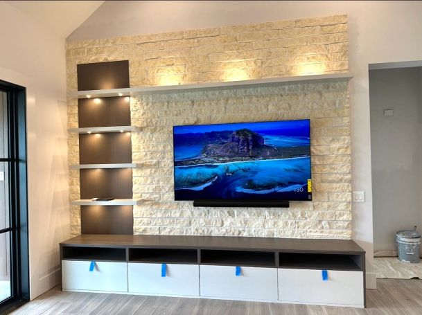 Flat screen television displaying an island landscape on a stone accent wall above a media console