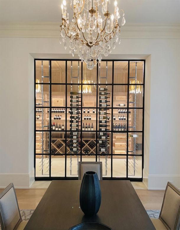 View from a dining room through a black metal paneled glass wall into a custom wine cellar