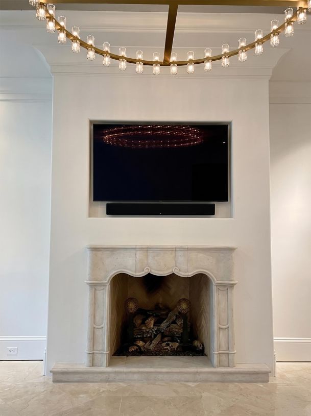 Flat screen television mounted over a classic stone fireplace under a round crystal chandelier